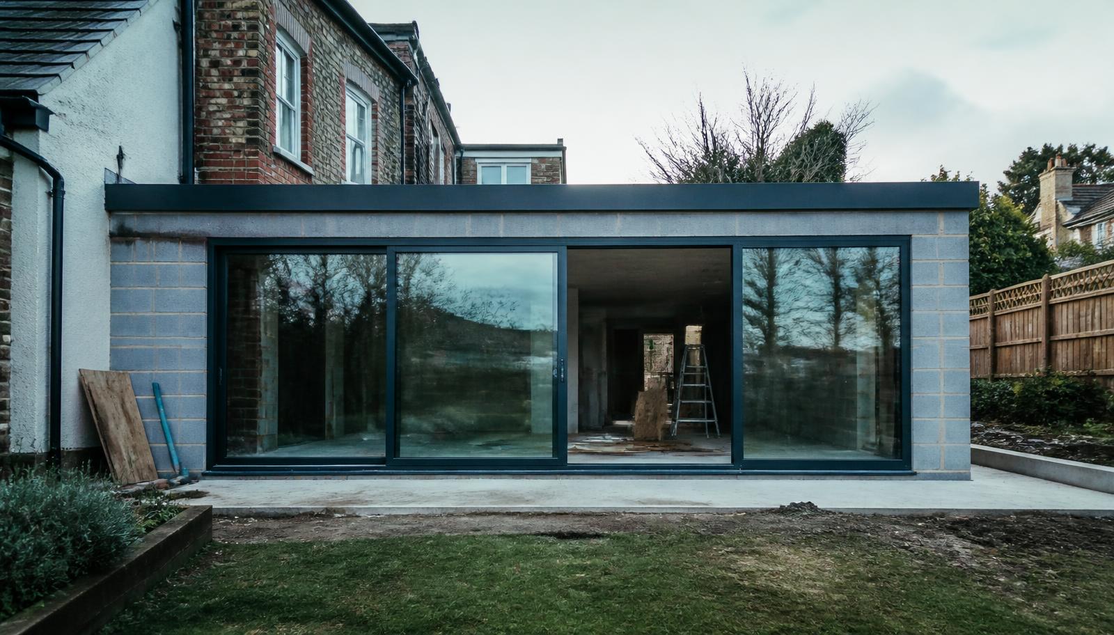 Modern single-storey rear extension under construction with large glazed sliding doors onto a garden